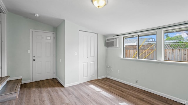 unfurnished bedroom featuring a wall mounted air conditioner, lofted ceiling, wood finished floors, a closet, and baseboards