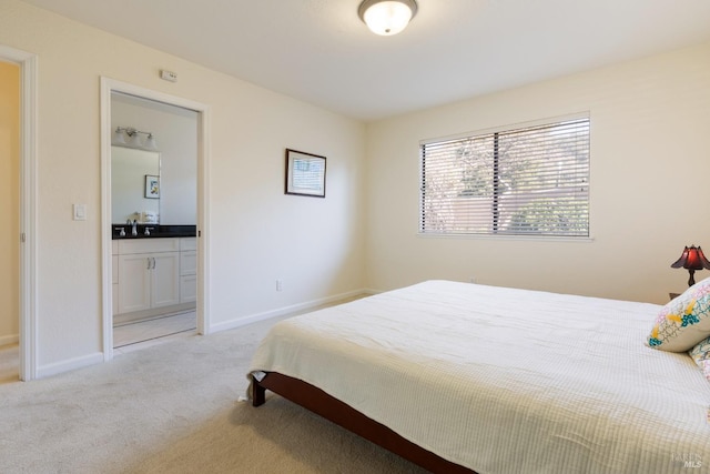 bedroom featuring light carpet, a sink, baseboards, and ensuite bathroom