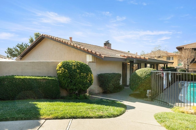 exterior space featuring a lawn, a tile roof, a chimney, fence, and stucco siding