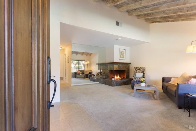 living area featuring a tile fireplace, light carpet, visible vents, a towering ceiling, and beamed ceiling