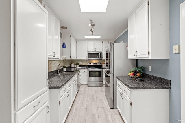 kitchen with stainless steel appliances, a skylight, white cabinetry, and a sink