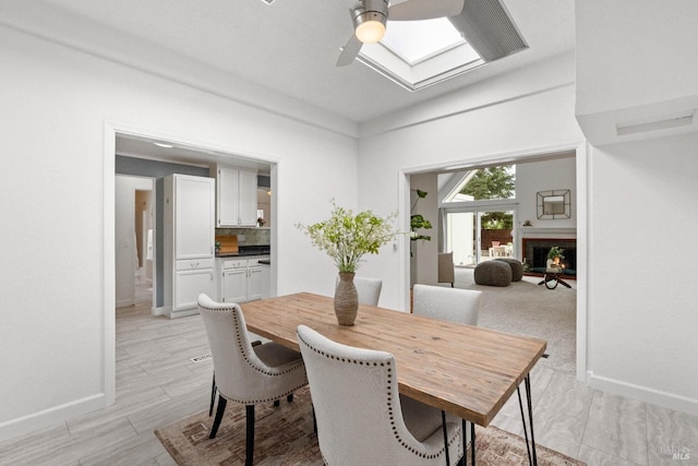 dining room featuring a warm lit fireplace, baseboards, and a skylight