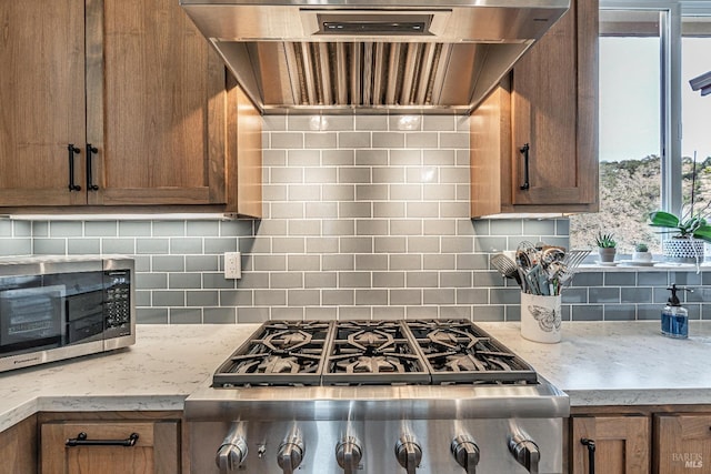 kitchen with stainless steel appliances, a center island, backsplash, glass insert cabinets, and wall chimney range hood
