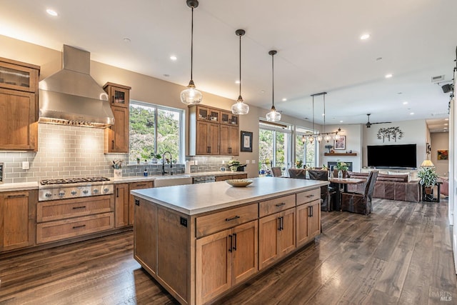 kitchen with backsplash, exhaust hood, light stone countertops, brown cabinetry, and appliances with stainless steel finishes
