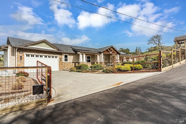 view of front of home featuring an attached garage, solar panels, driveway, stone siding, and a gate