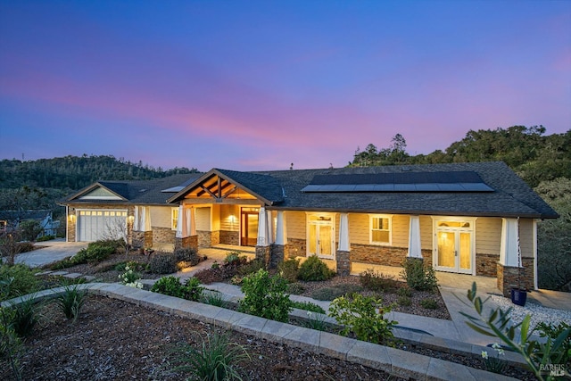 view of front of house with a gate, roof mounted solar panels, a forest view, and a fenced front yard