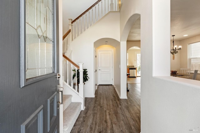 foyer entrance featuring dark wood finished floors, stairway, a high ceiling, a chandelier, and baseboards