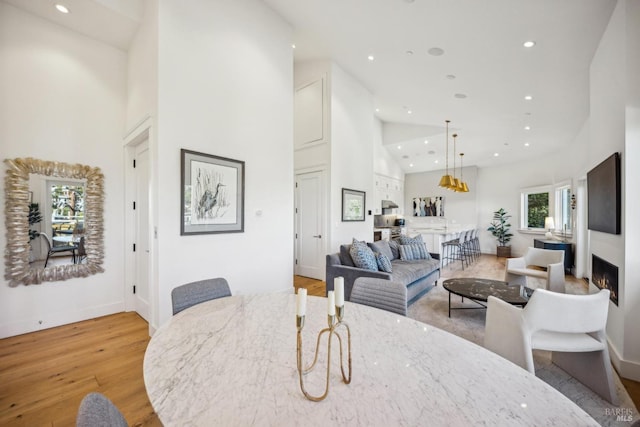 dining room with a lit fireplace, light wood-style flooring, high vaulted ceiling, and recessed lighting