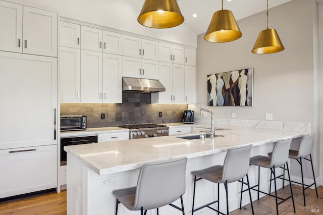 kitchen with range, a peninsula, under cabinet range hood, white cabinetry, and a sink