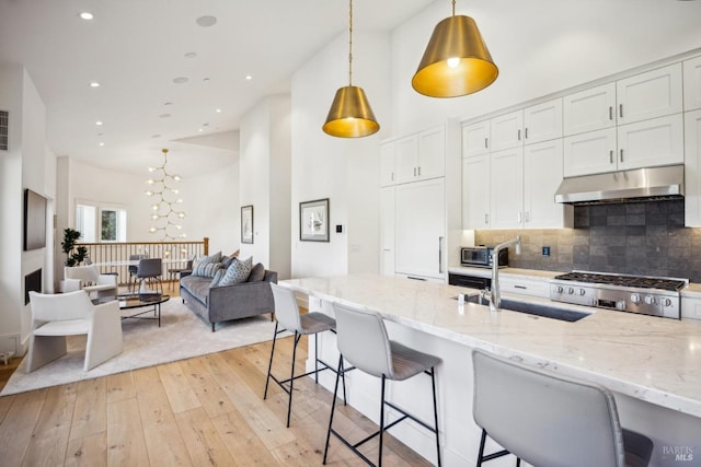 kitchen featuring decorative backsplash, a kitchen bar, a sink, and under cabinet range hood