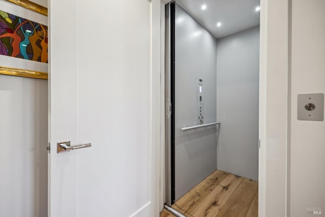 bathroom featuring elevator, wood finished floors, and recessed lighting