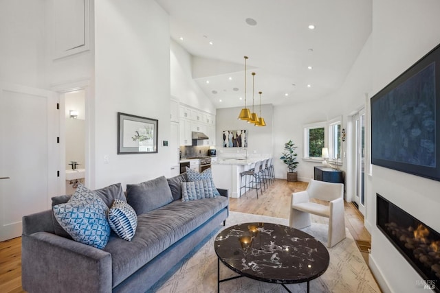 living room with high vaulted ceiling, light wood-type flooring, a glass covered fireplace, and recessed lighting