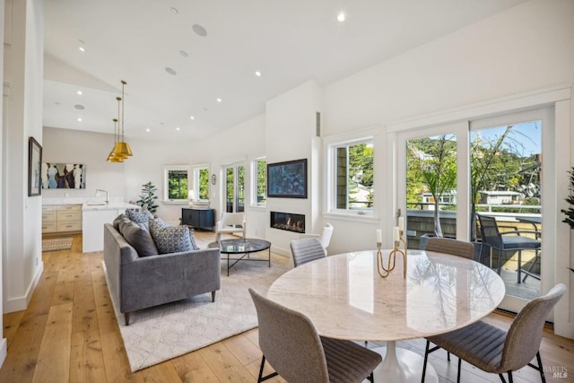 dining area featuring light wood-type flooring, recessed lighting, high vaulted ceiling, and a glass covered fireplace