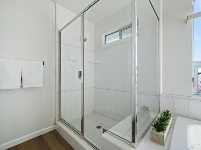 bathroom featuring a stall shower, wood finished floors, a bath, and baseboards