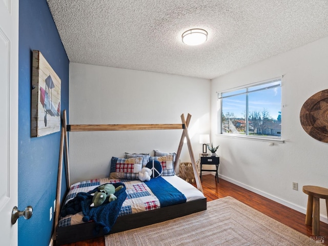 bedroom with a textured ceiling, baseboards, and wood finished floors