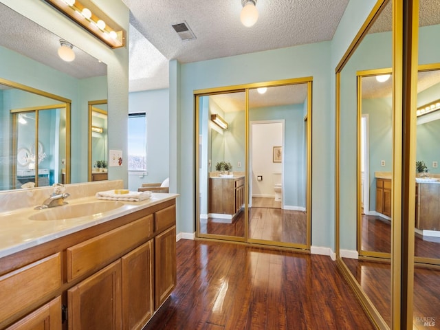 full bathroom with toilet, vanity, hardwood / wood-style flooring, a textured ceiling, and visible vents