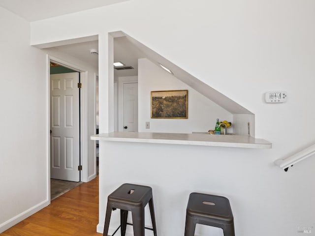 kitchen featuring a breakfast bar, light countertops, wood finished floors, a peninsula, and baseboards