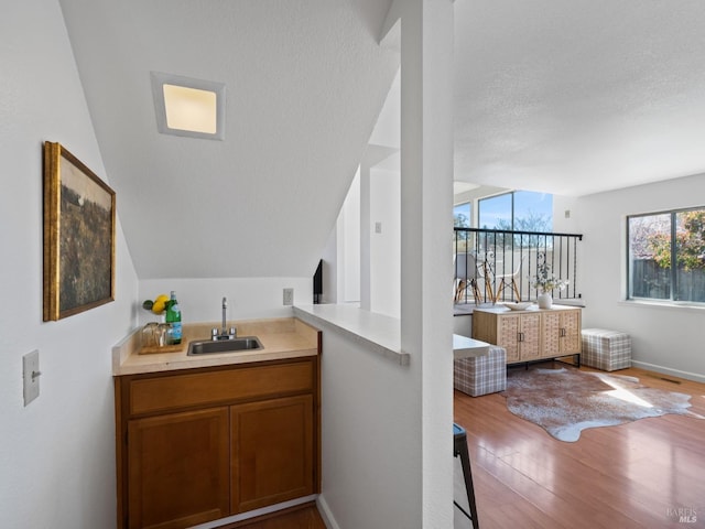 bar featuring a textured ceiling, baseboards, wood finished floors, a sink, and vaulted ceiling