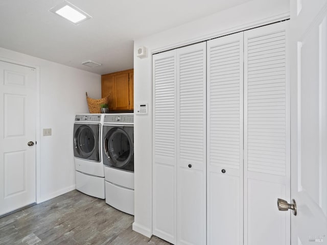 clothes washing area featuring washing machine and clothes dryer, cabinet space, baseboards, and light wood-type flooring