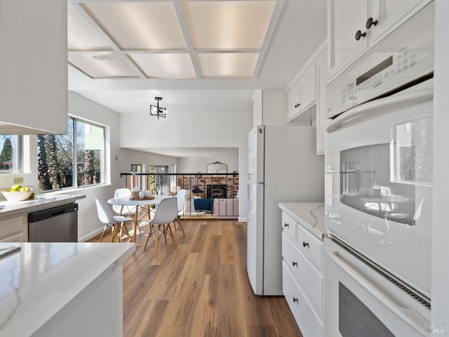 kitchen with light stone counters, a fireplace, white cabinetry, wood finished floors, and white appliances