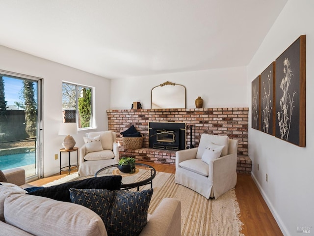 living area featuring a brick fireplace, baseboards, and wood finished floors
