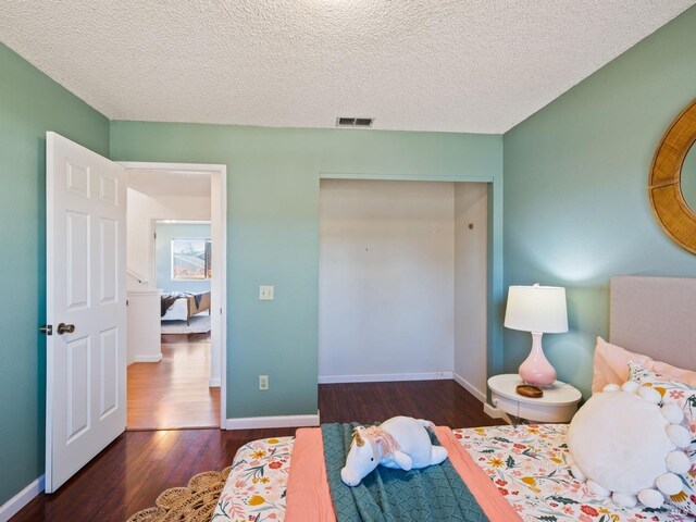 bedroom with a textured ceiling, wood finished floors, visible vents, and baseboards