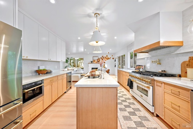 kitchen with light brown cabinets, light wood-style flooring, stainless steel appliances, a center island, and custom range hood