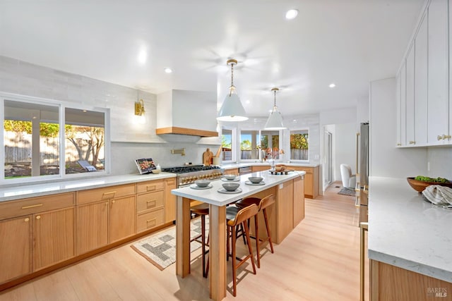 kitchen featuring wall chimney exhaust hood, a kitchen island, light wood-style flooring, and a wealth of natural light