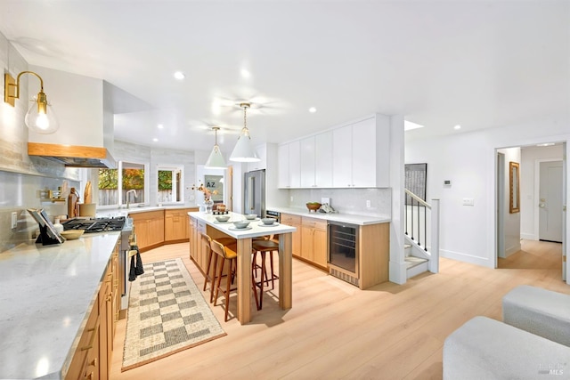 kitchen featuring a breakfast bar, tasteful backsplash, light wood-type flooring, beverage cooler, and stainless steel gas range oven