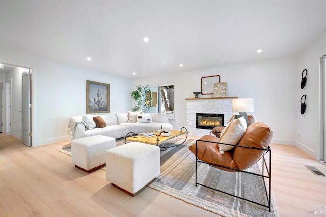 living area featuring visible vents, baseboards, a stone fireplace, light wood-style floors, and recessed lighting