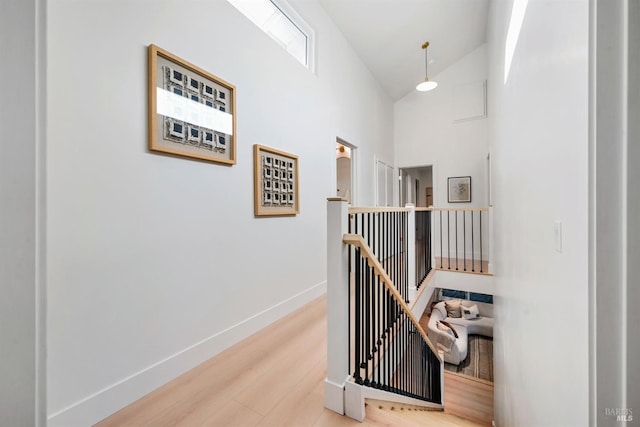 corridor with high vaulted ceiling, baseboards, wood finished floors, and an upstairs landing