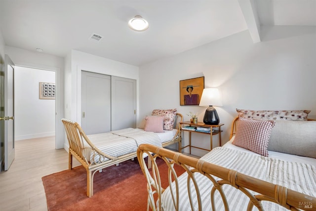 bedroom with light wood finished floors, a closet, visible vents, lofted ceiling with beams, and baseboards