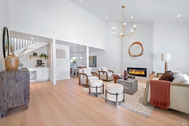 living area with light wood-style floors, a tile fireplace, a towering ceiling, and a notable chandelier