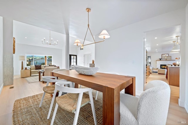 dining space with an inviting chandelier, visible vents, light wood finished floors, and a stone fireplace