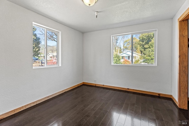 unfurnished room with dark wood-style floors, a healthy amount of sunlight, a textured ceiling, and baseboards