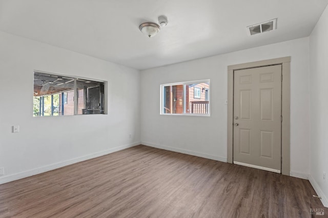 empty room featuring a healthy amount of sunlight, visible vents, baseboards, and wood finished floors