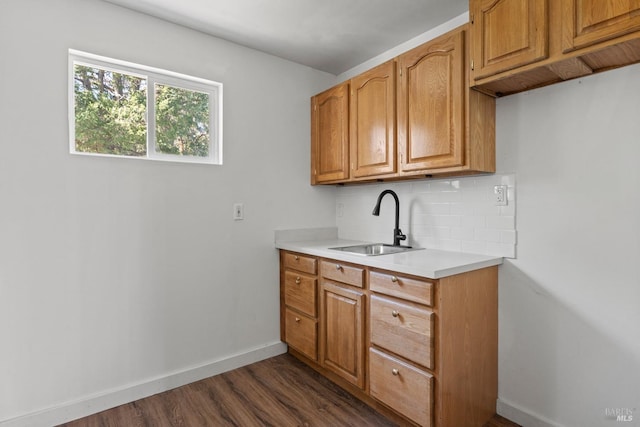 kitchen featuring tasteful backsplash, baseboards, dark wood-type flooring, light countertops, and a sink