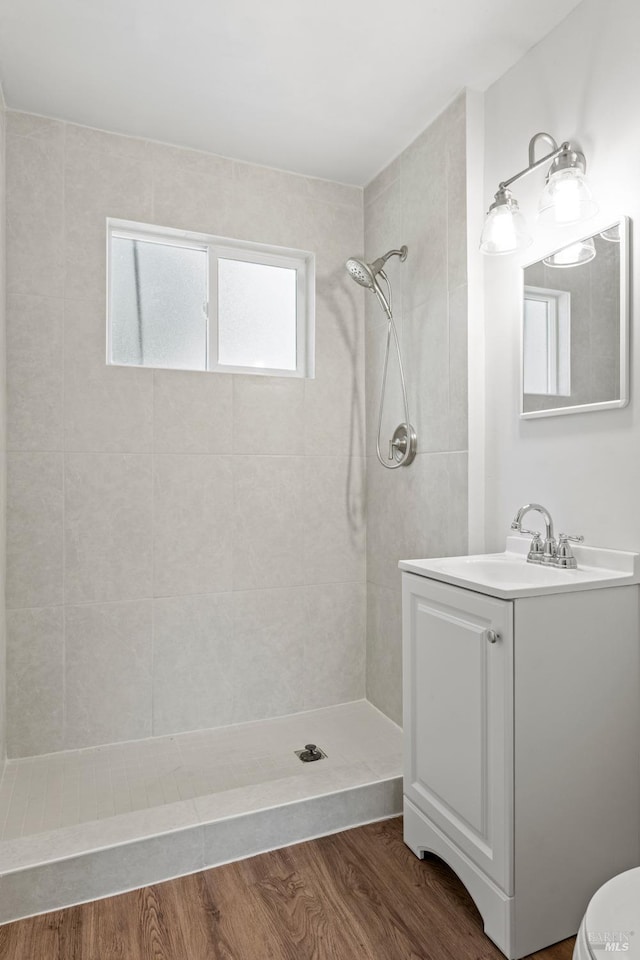 bathroom with a tile shower, toilet, wood finished floors, and vanity