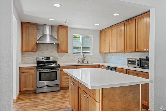 kitchen featuring stainless steel range with gas cooktop, light wood finished floors, light countertops, a sink, and wall chimney exhaust hood