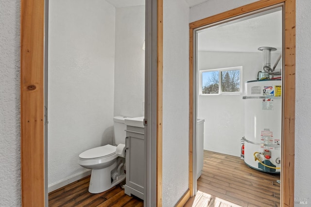 bathroom with toilet, wood finished floors, vanity, baseboards, and strapped water heater