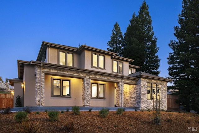 view of front of house featuring stone siding, stucco siding, a porch, and fence