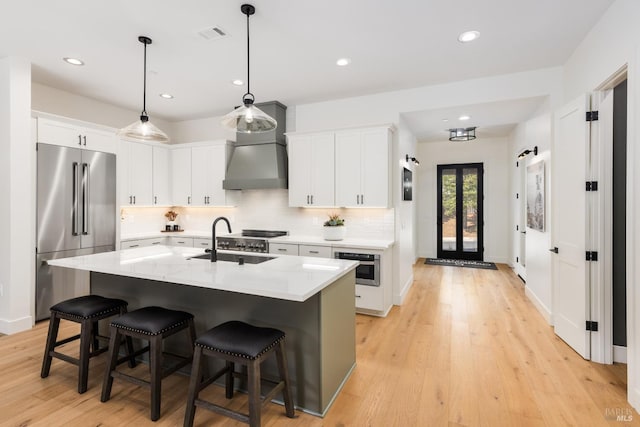 kitchen featuring light wood finished floors, high end fridge, a sink, light countertops, and tasteful backsplash