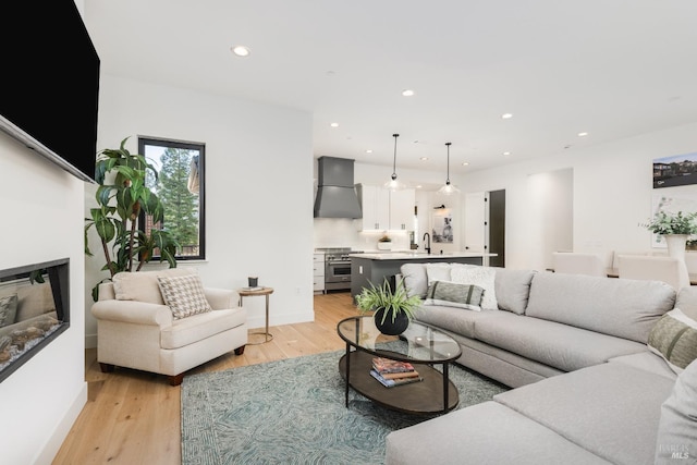 living area with a glass covered fireplace, light wood-style flooring, recessed lighting, and baseboards