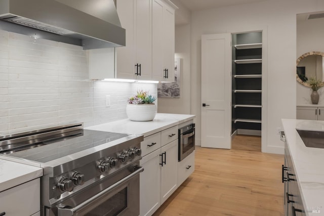 kitchen featuring visible vents, wall chimney exhaust hood, light wood finished floors, decorative backsplash, and high end range