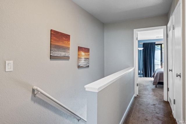 hallway with dark carpet, an upstairs landing, and baseboards