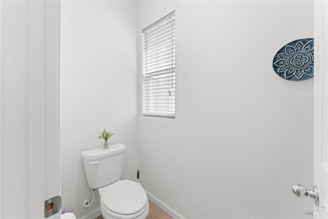 bathroom featuring toilet, baseboards, and a healthy amount of sunlight