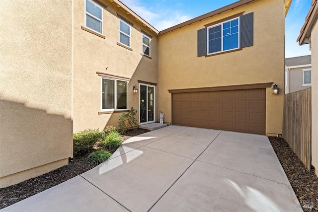 view of front of house featuring concrete driveway, a garage, stucco siding, and fence