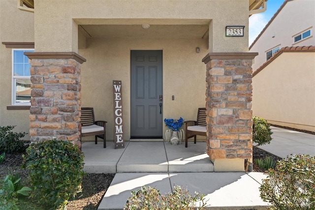 property entrance featuring a porch, stone siding, and stucco siding