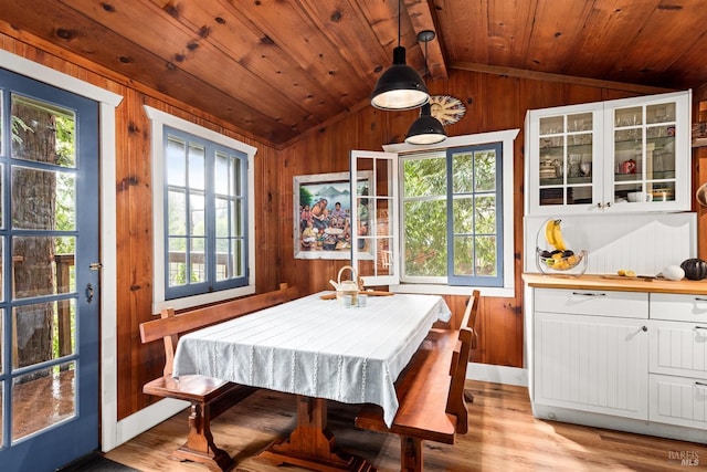 dining area featuring vaulted ceiling, light wood finished floors, wood ceiling, and wooden walls