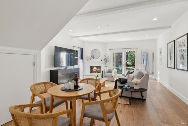 dining room featuring a warm lit fireplace, baseboards, light wood-type flooring, beam ceiling, and recessed lighting